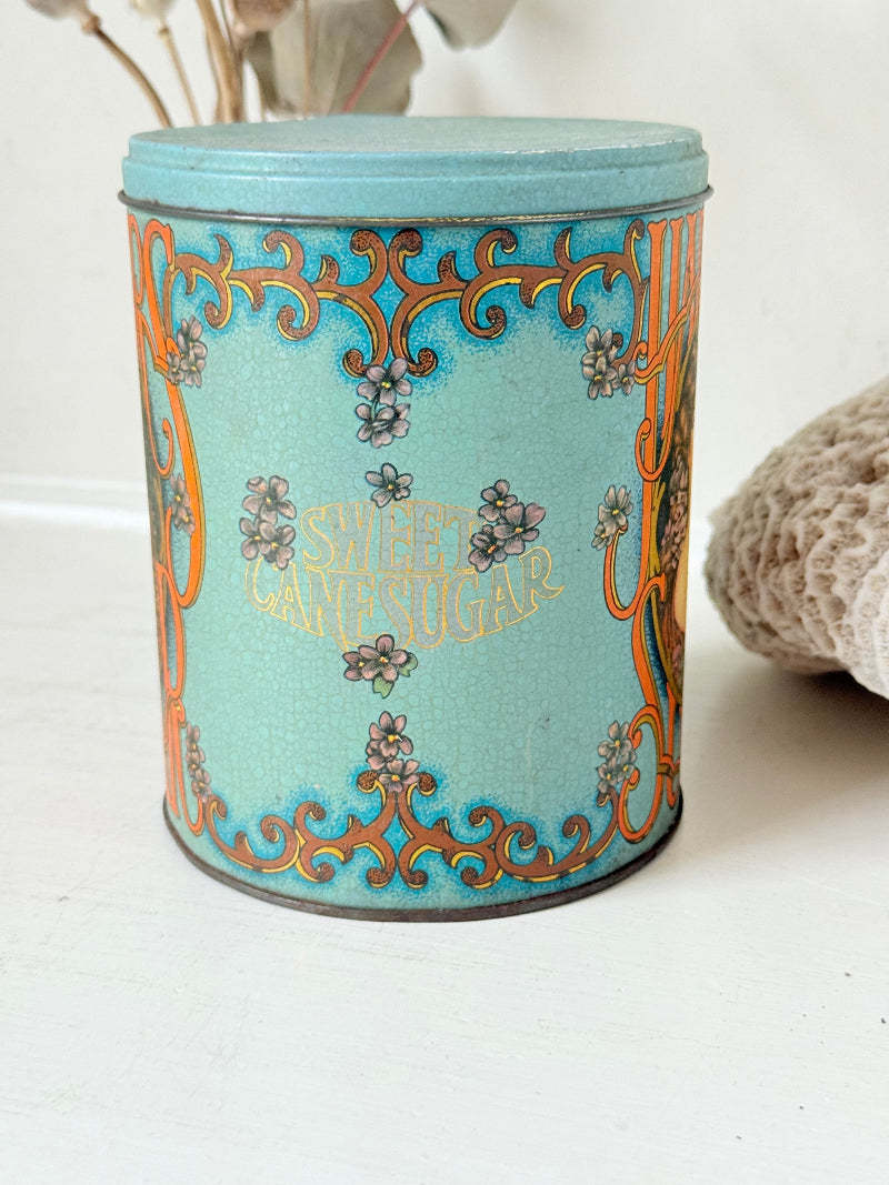 Vintage turquoise and gold metal sweet tin with Art Nouveau woman portrait photographed on a white surface.