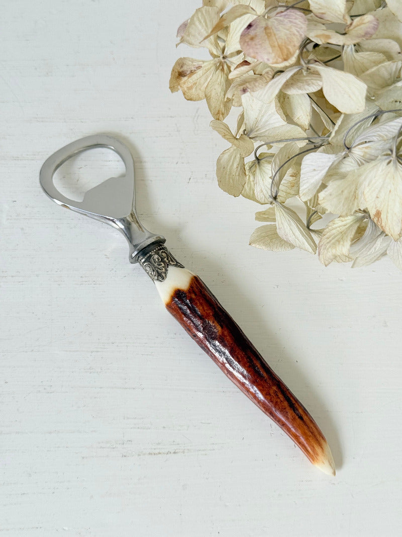 vintage antler handle bottle opener with stainless steel top photographed on white surface