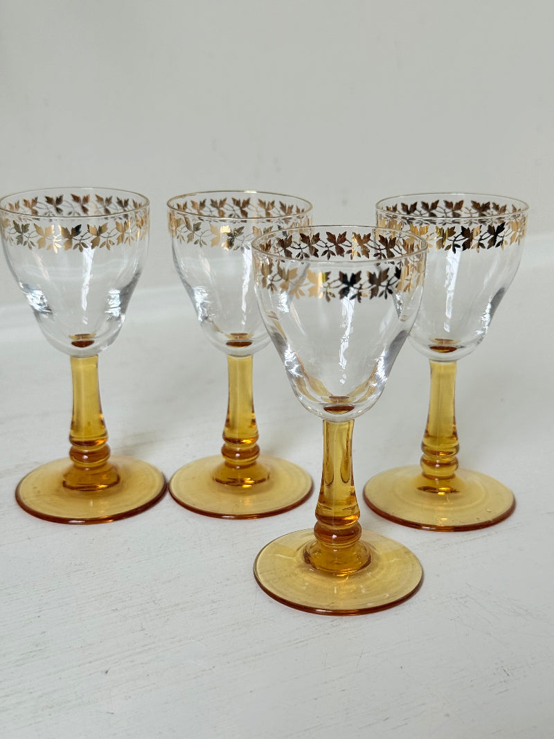 Vintage set of four shot glasses with amber stems and gilt rims, photographed on a white surface