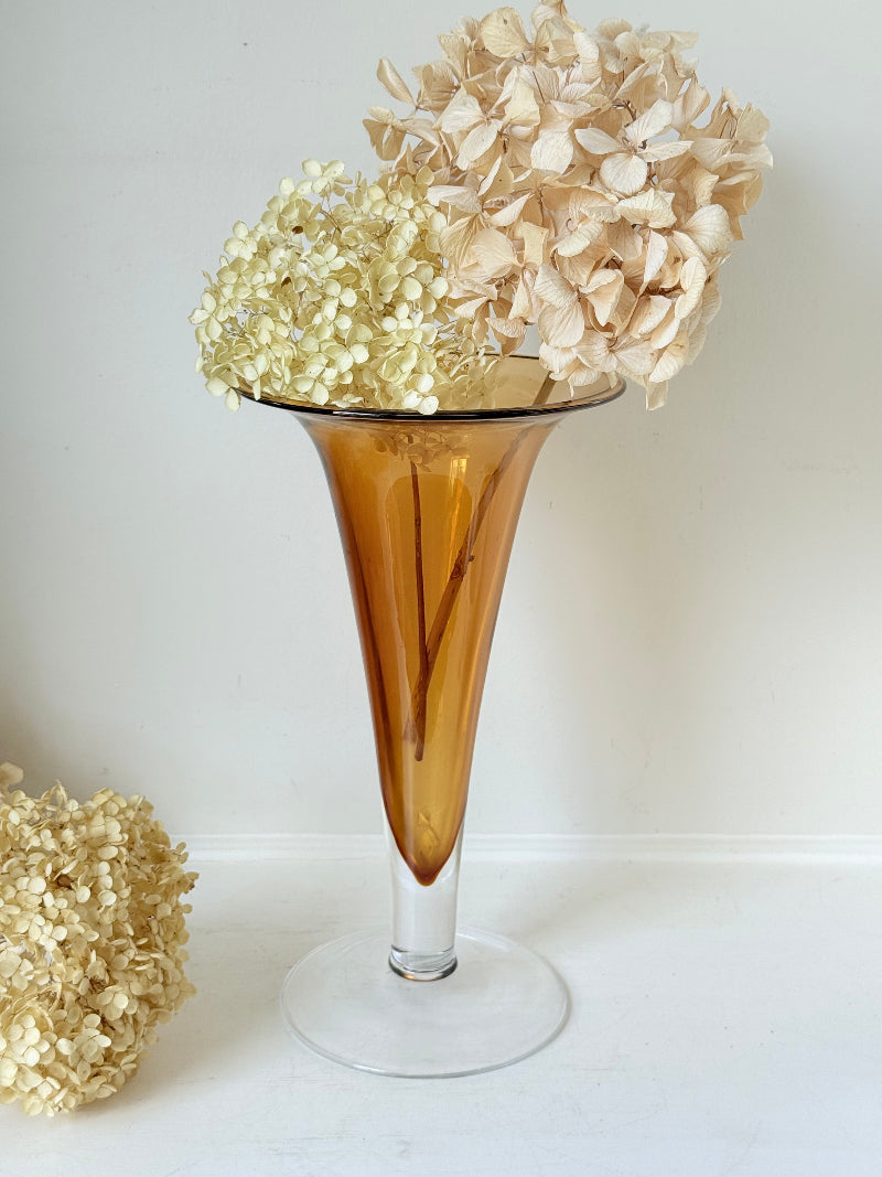 Tall mid-century amber trumpet vase with flared rim and clear glass foot, styled against a neutral background