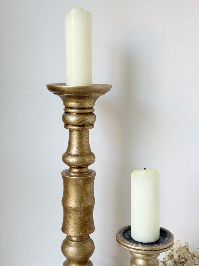 Pair of vintage wooden candlesticks, one tall and one small, in golden-toned finish, styled with pillar candles on a white surface.