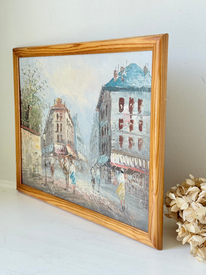 Vintage oil painting of European street scene with buildings and awnings in wooden frame photographed on a white surface