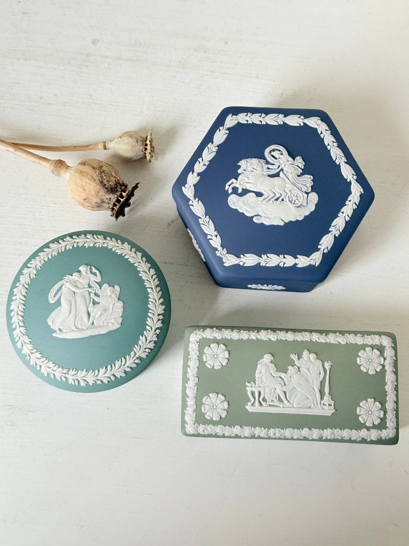 Trio of vintage Wedgwood Jasperware lidded pots in Portland blue and sage green, featuring neoclassical white relief figures, styled with dried stems on a pale surface.
