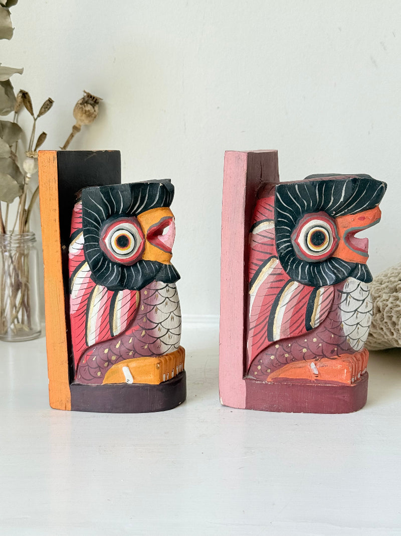 Vintage wooden owl bookends hand painted in red and orange tones, displayed on a white surface beside dried flowers.