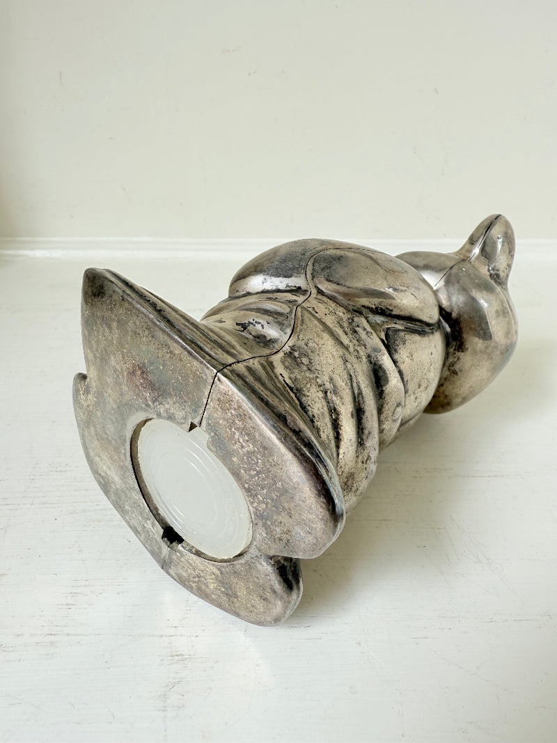 Vintage silver tone metal bear money box with coin slot on top, photographed on a white surface.