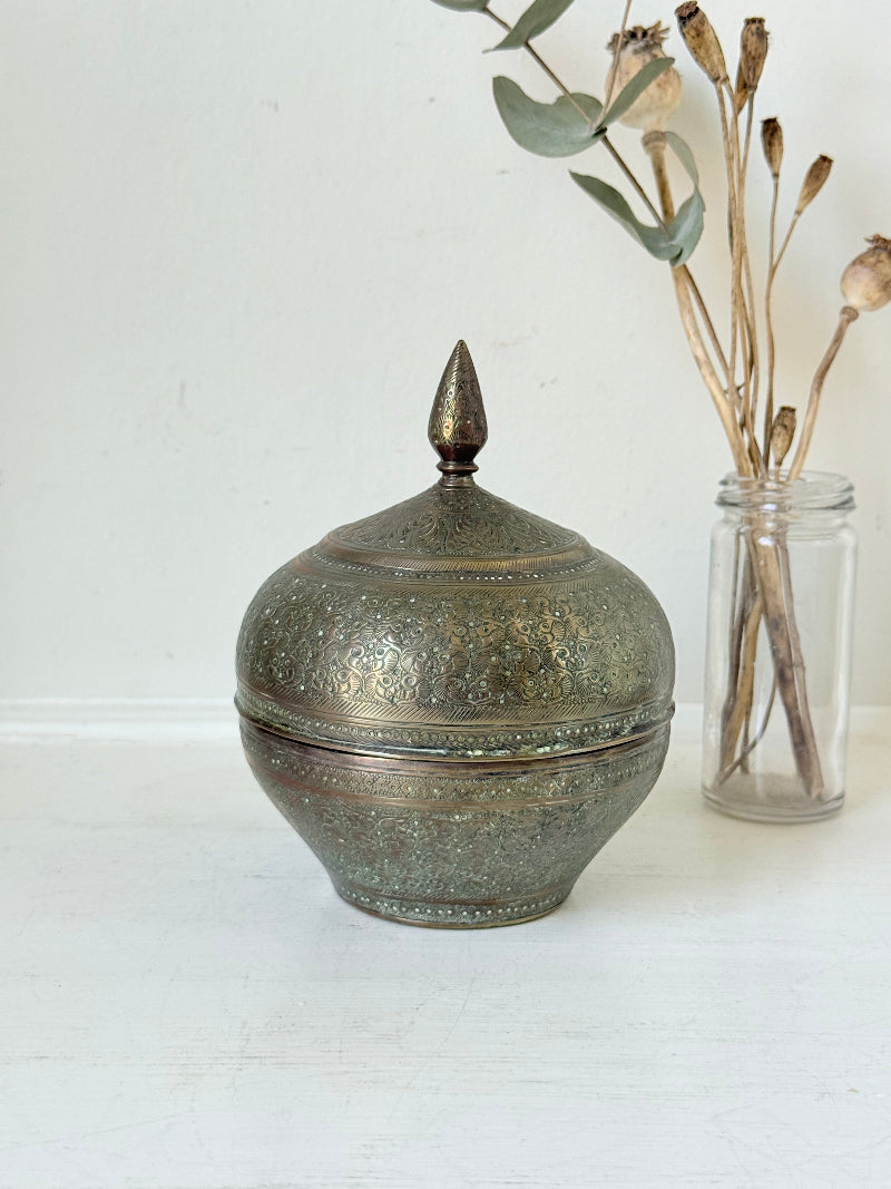 Indian Benares brass lidded jar with floral engraving and finial, photographed on a white surface