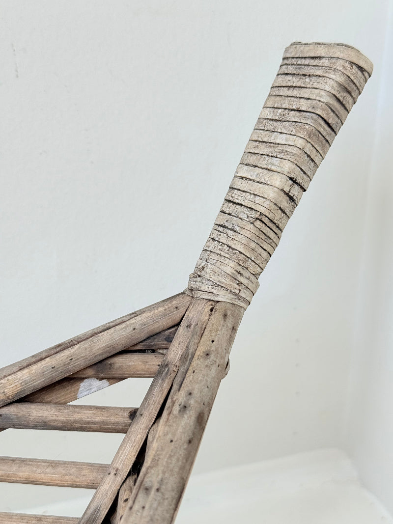 Large curved woven basket with slatted sides and repaired plywood base photographed on a white surface