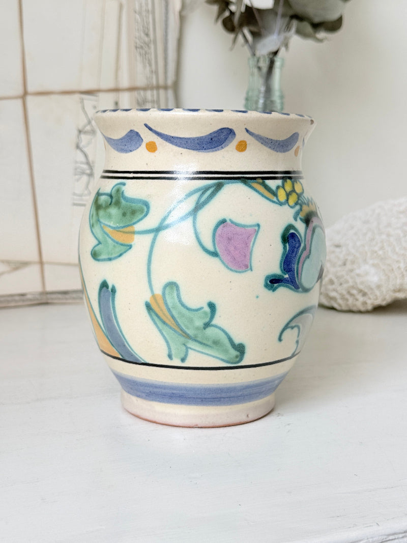 Hand painted floral pottery vase in blue and green on cream, photographed on a white surface