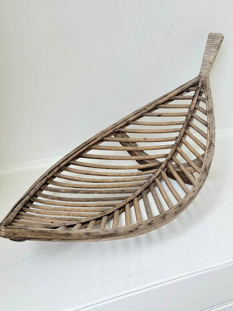 Large curved woven basket with slatted sides and repaired plywood base photographed on a white surface