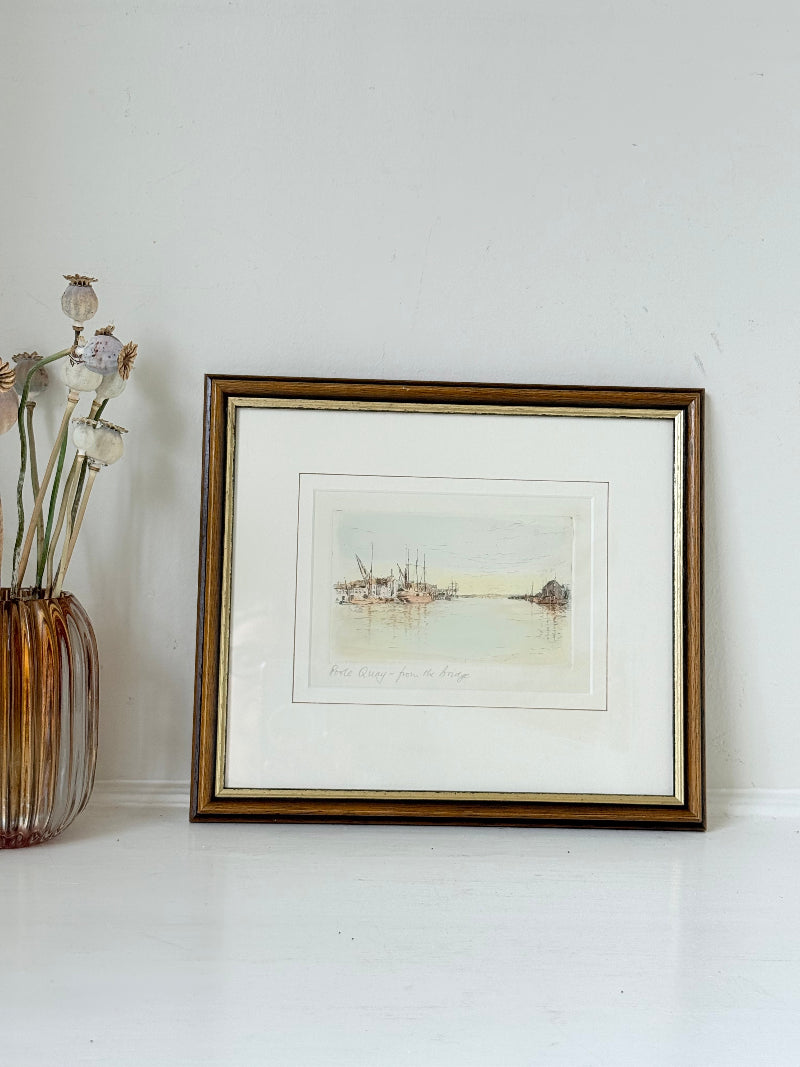 Framed vintage print of Poole Quay harbour scene in muted tones, under glass with gilt and wood-effect frame, on white surface.