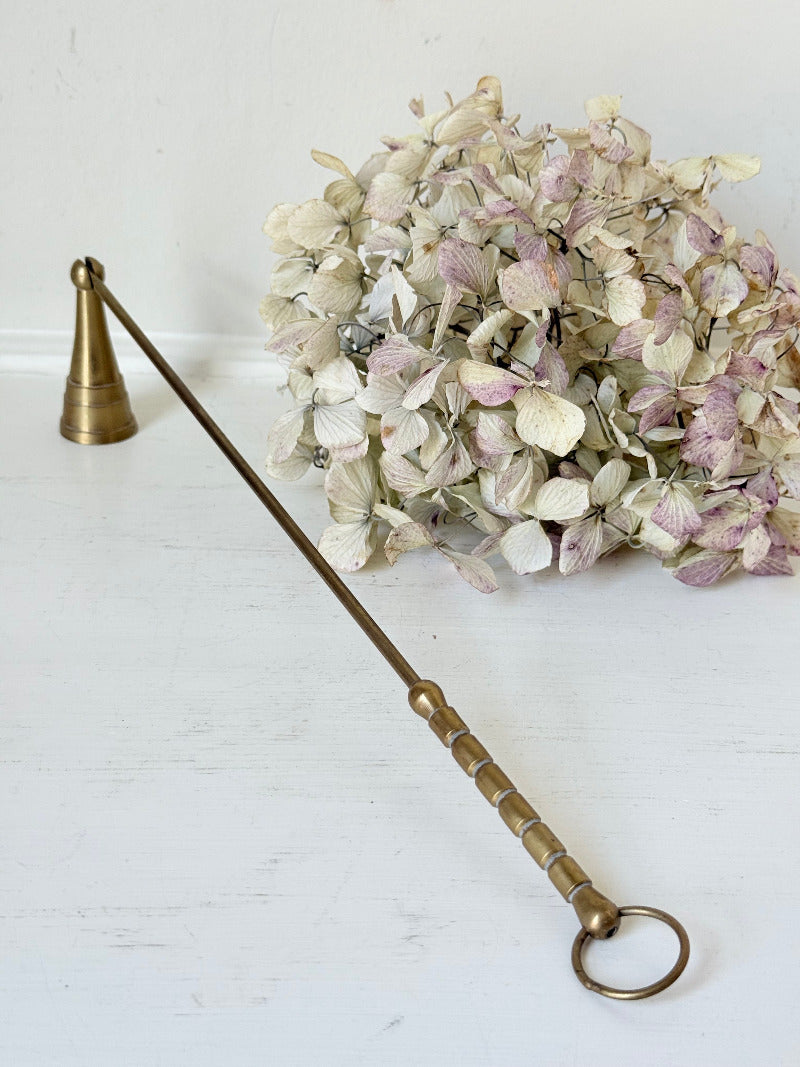 vintage brass candle snuffer with twisted handle and cone-shaped head photographed on white surface
