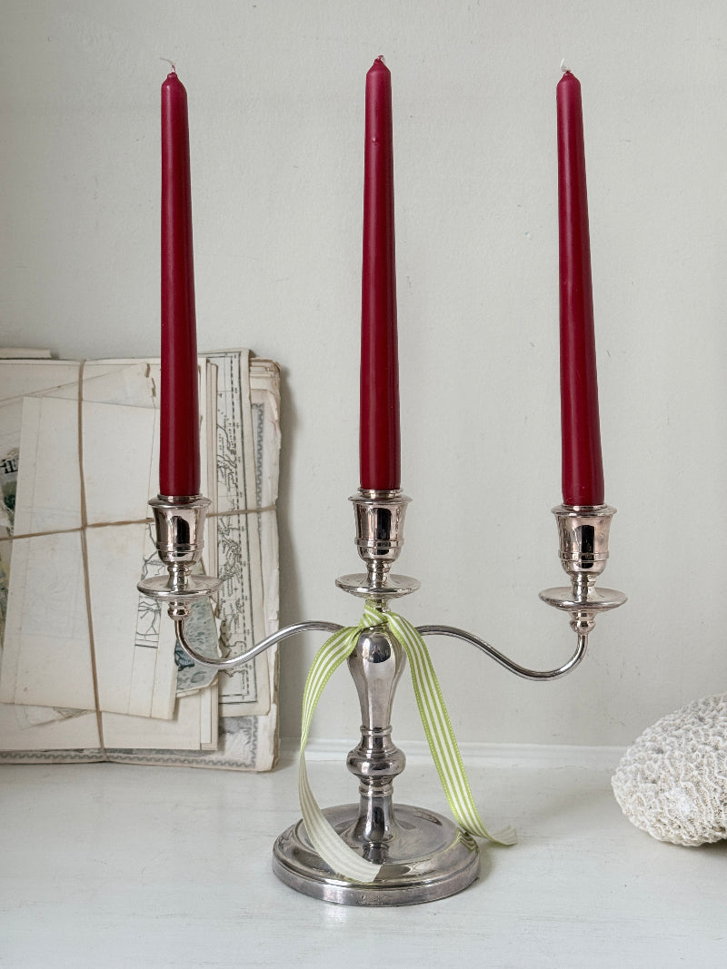 Silver plate three light candelabra with curved arms and domed base holding red taper candles