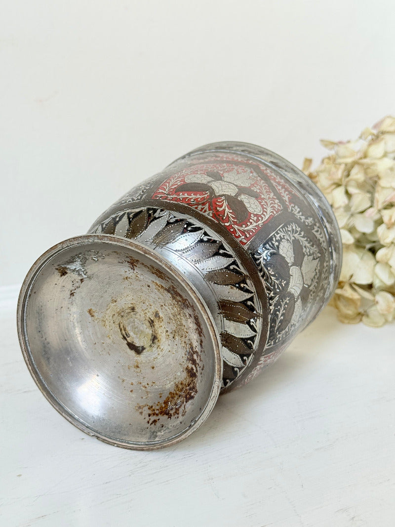 vintage indian metal lassi cup with red and white enamel motifs, styled with dried hydrangeas on a white surface