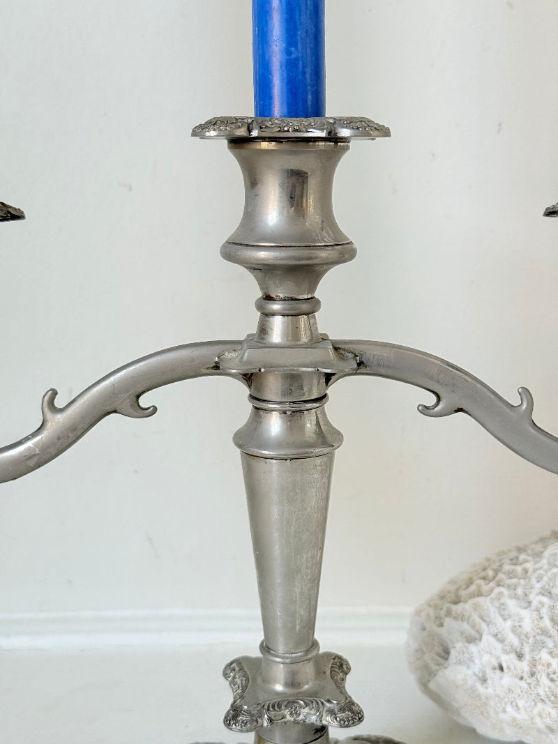 Vintage silver coloured three-arm candelabra with ornate base and soft patina, photographed on a white surface
