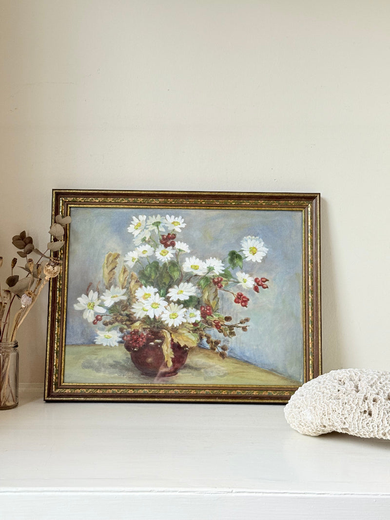 Vintage oil painting on board of daisies in a vase, framed under glass and photographed on a white surface beside dried flowers.