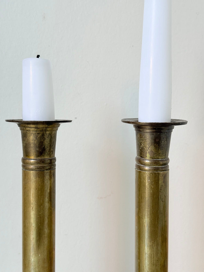 Pair of vintage brass candlesticks with square bases and white taper candles, styled on a white surface beside dried hydrangeas.