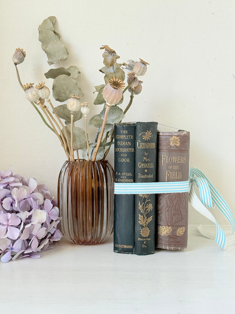 Bundle of antique books with decorative spines tied with ribbon, styled on white surface with dried flowers