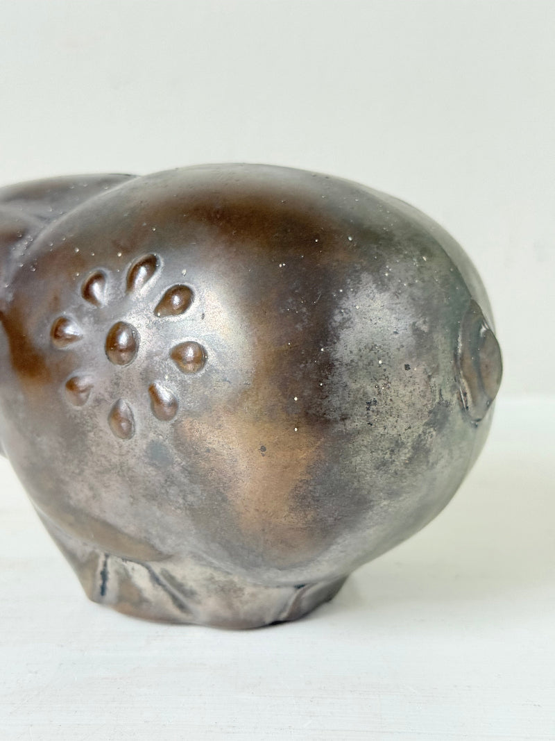 Vintage cast metal piggy bank in the shape of a pig with red painted eyes, photographed on a white surface