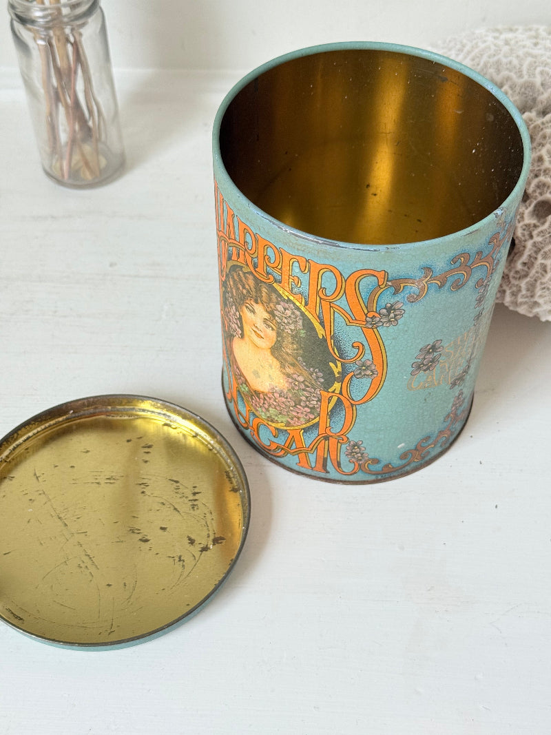 Vintage turquoise and gold metal sweet tin with Art Nouveau woman portrait photographed on a white surface.