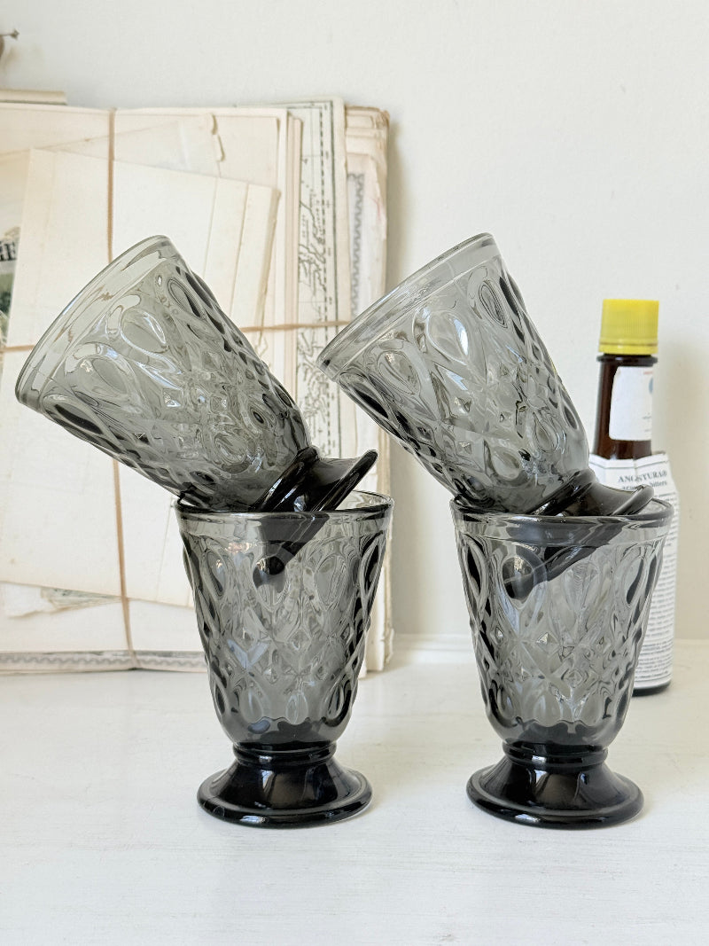 Set of four smoke grey pressed glass footed goblets with a diamond pattern, photographed on a white surface