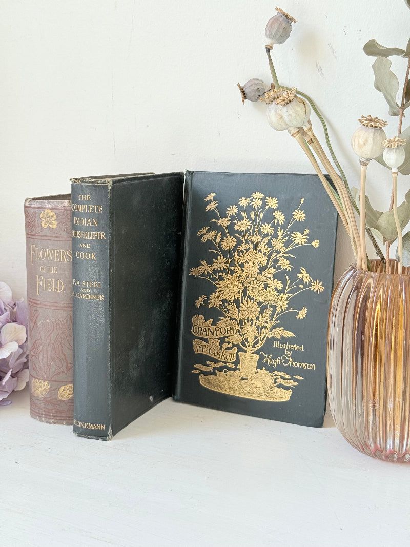 Bundle of antique books with decorative spines tied with ribbon, styled on white surface with dried flowers