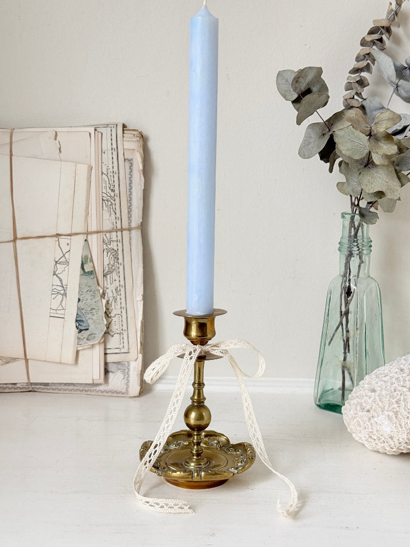 Brass candlestick with turned baluster stem and scalloped embossed base photographed on a white surface