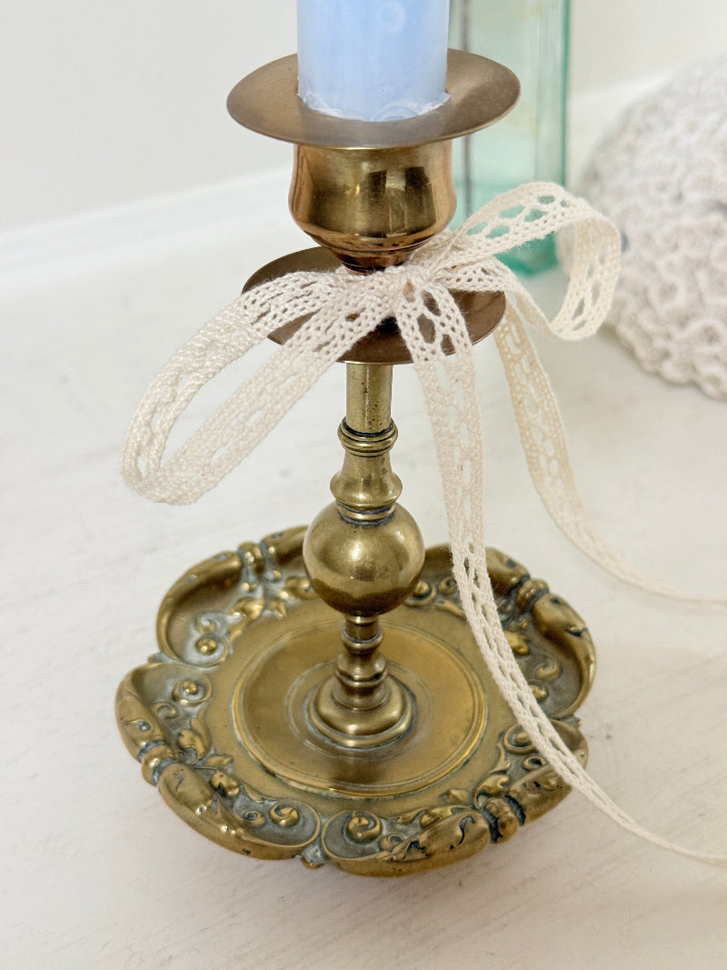 Brass candlestick with turned baluster stem and scalloped embossed base photographed on a white surface