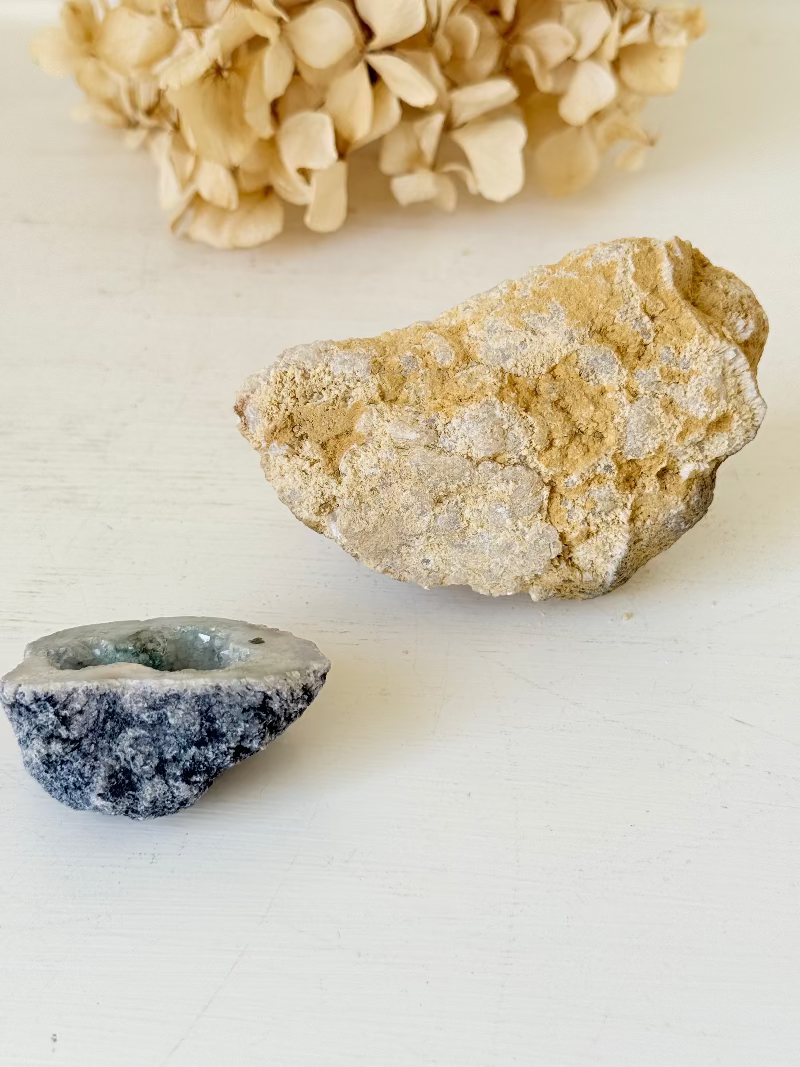 Pair of natural quartz geodes, one white and one lilac-toned, styled on a white surface with dried hydrangea