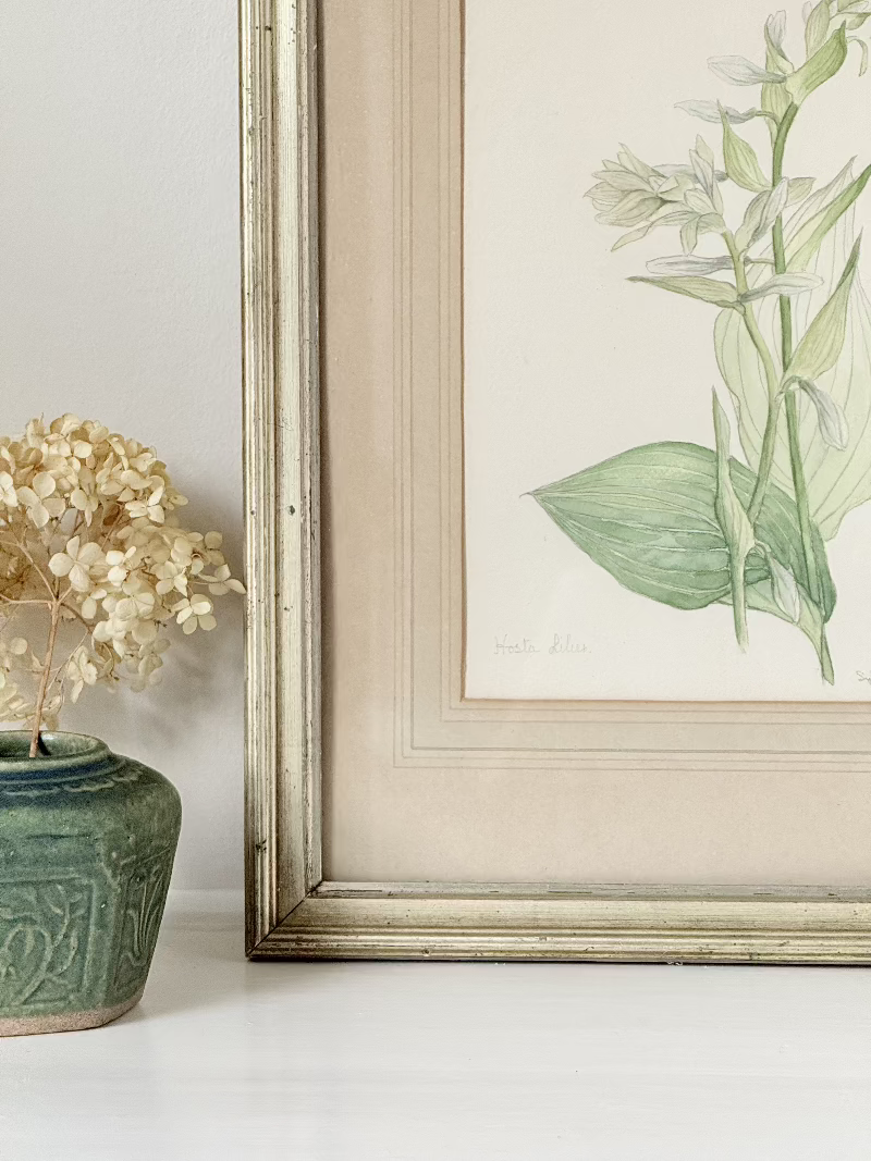 Vintage watercolour of hosta lilies in a gilt frame, signed and dated 1974, styled on white surface with soft decor