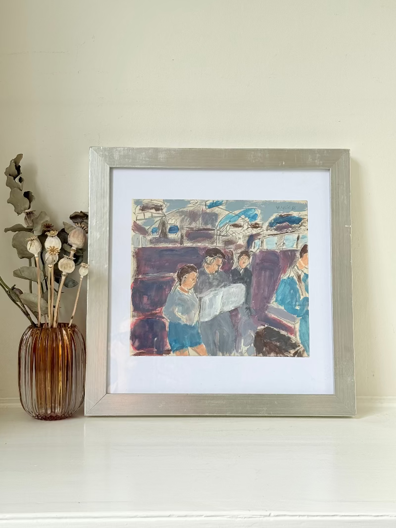 Mixed media painting by Watkiss of figures in a train carriage, framed in white, photographed on a white surface