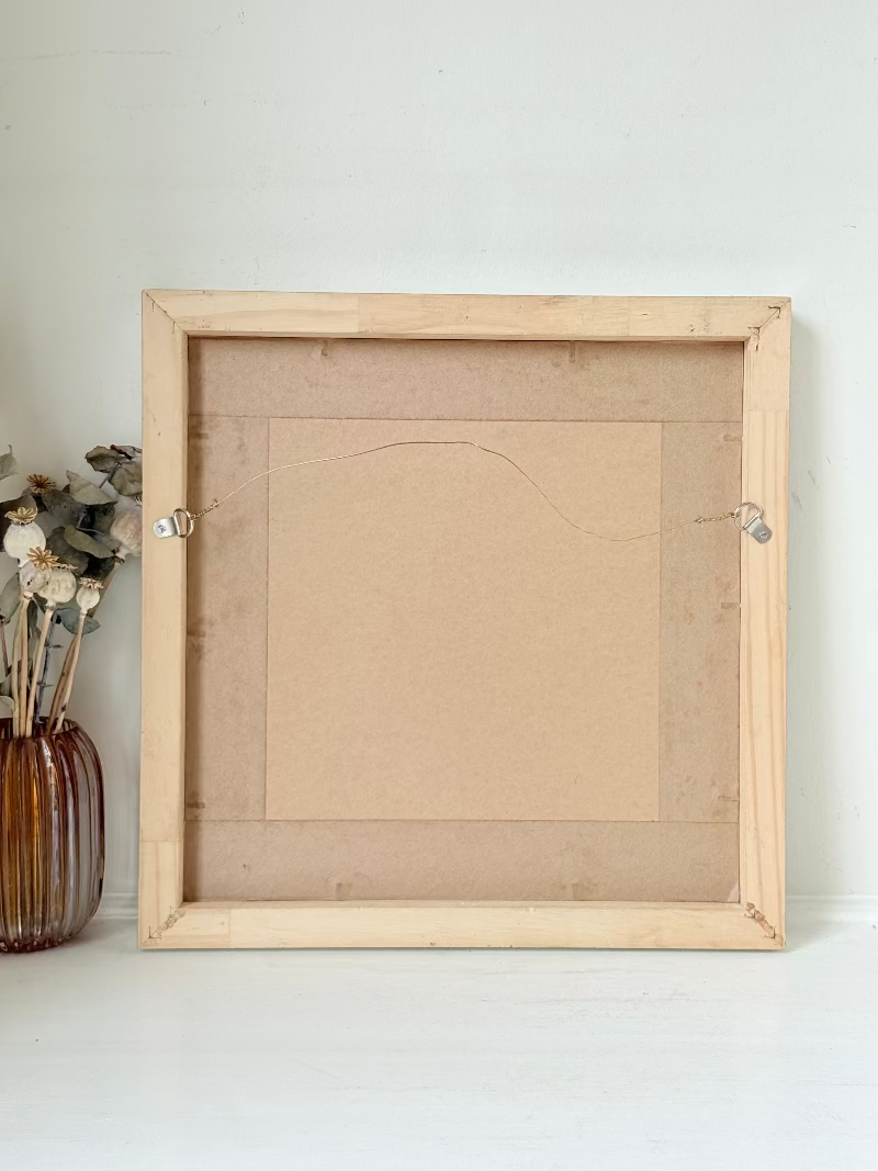Mixed media painting by Watkiss of figures in a train carriage, framed in white, photographed on a white surface