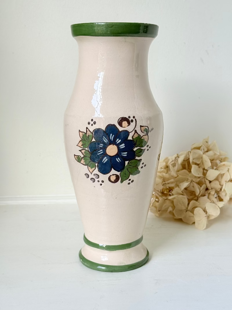 Vintage studio pottery vase with hand painted blue floral design and green glazed rim and foot, photographed on white surface.