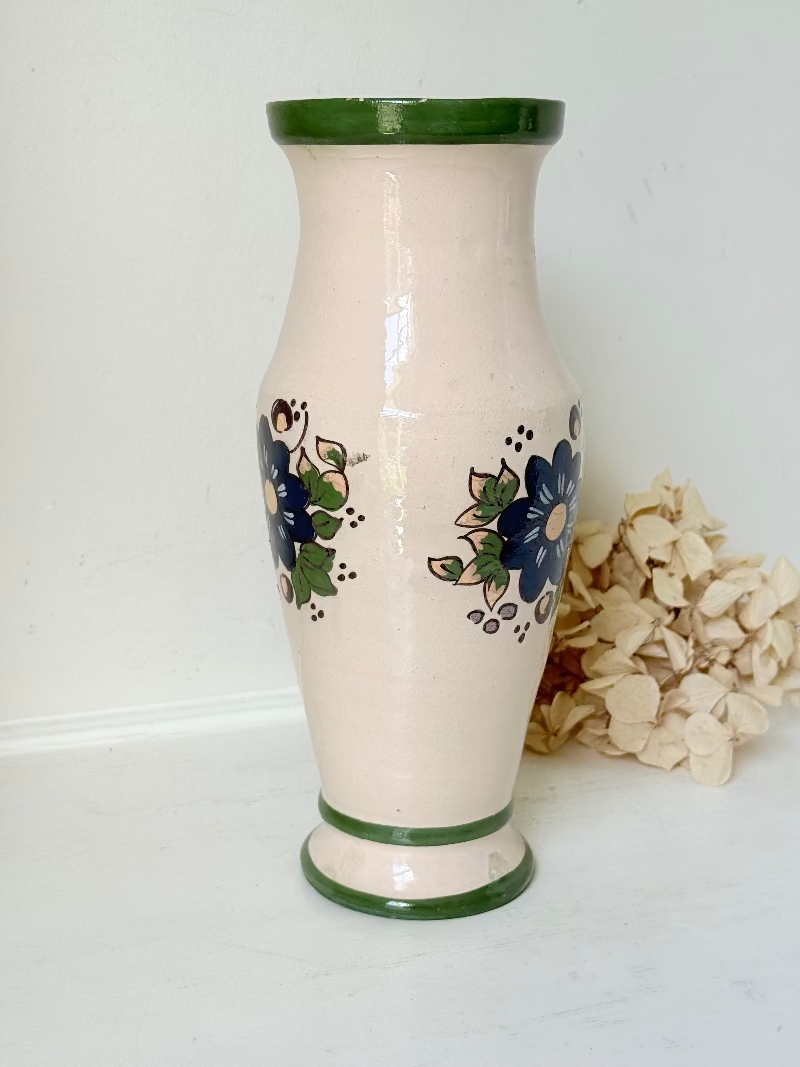 Vintage studio pottery vase with hand painted blue floral design and green glazed rim and foot, photographed on white surface.