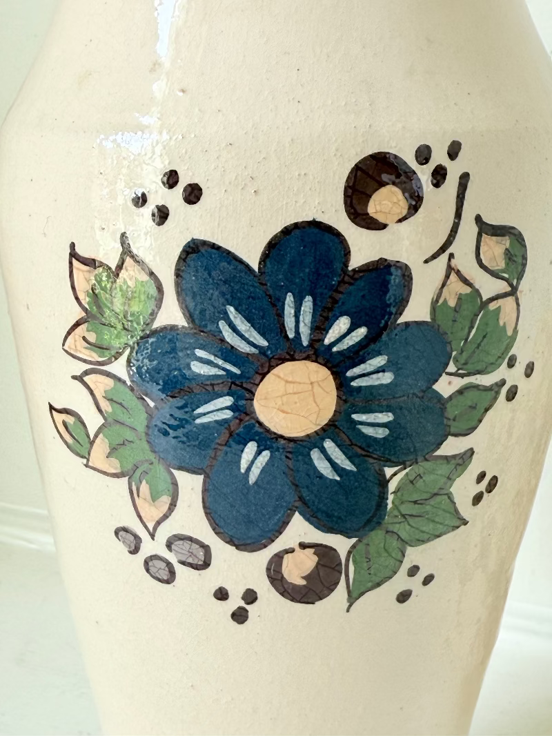 Vintage studio pottery vase with hand painted blue floral design and green glazed rim and foot, photographed on white surface.