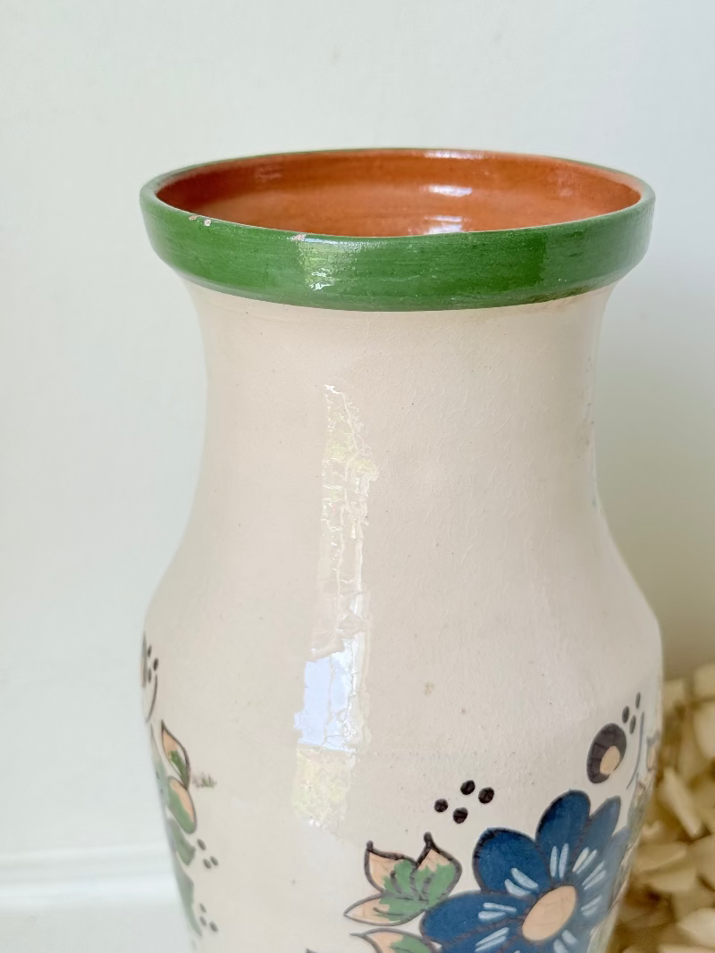 Vintage studio pottery vase with hand painted blue floral design and green glazed rim and foot, photographed on white surface.
