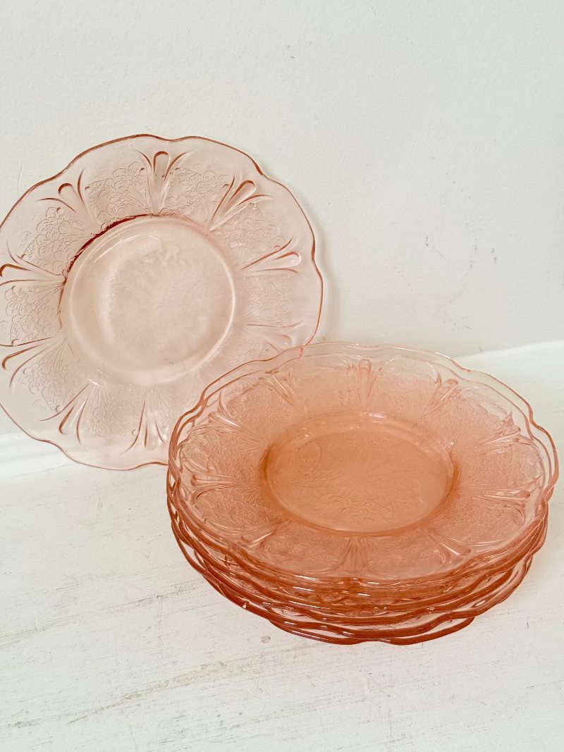 Set of seven vintage pressed glass coral plates with cherry and blossom motif, photographed on white surface.