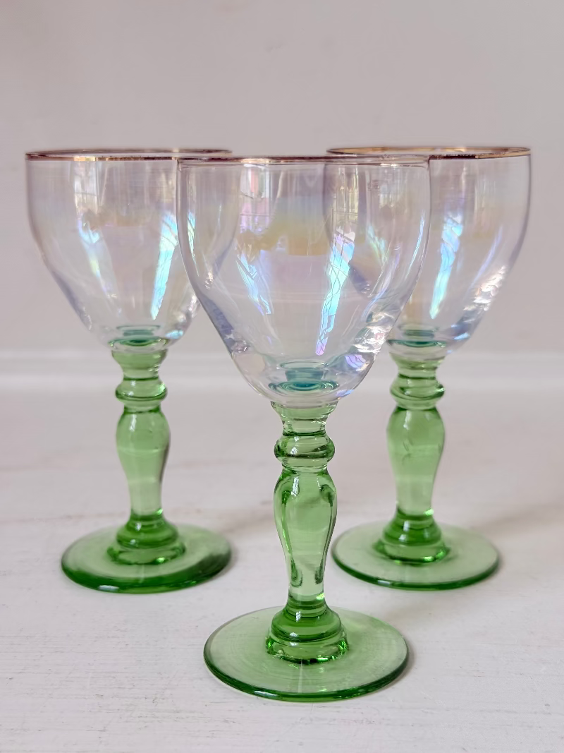 Vintage trio of iridescent shot glasses with green stems and gilt rims, photographed on a white surface
