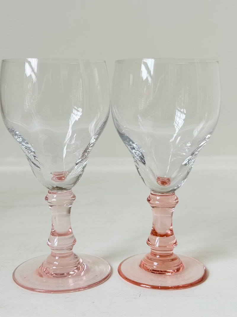 Set of three vintage liquor glasses with clear bowls and pink stems, one paler in tone, photographed on white surface.