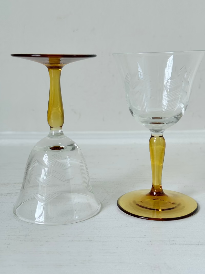 Pair of vintage liquor glasses with clear bowls and amber stems, photographed on white surface.