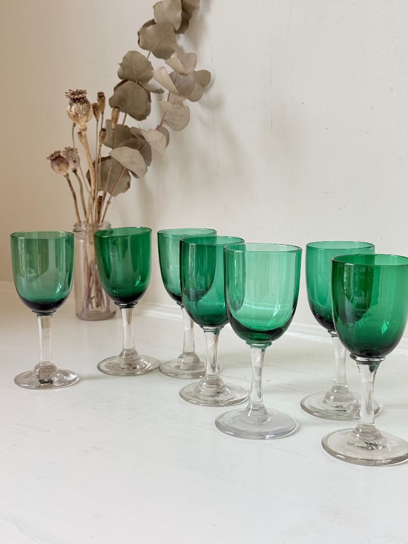 Set of seven antique Bristol green glasses with clear stems and emerald bowls, photographed on white surface.
