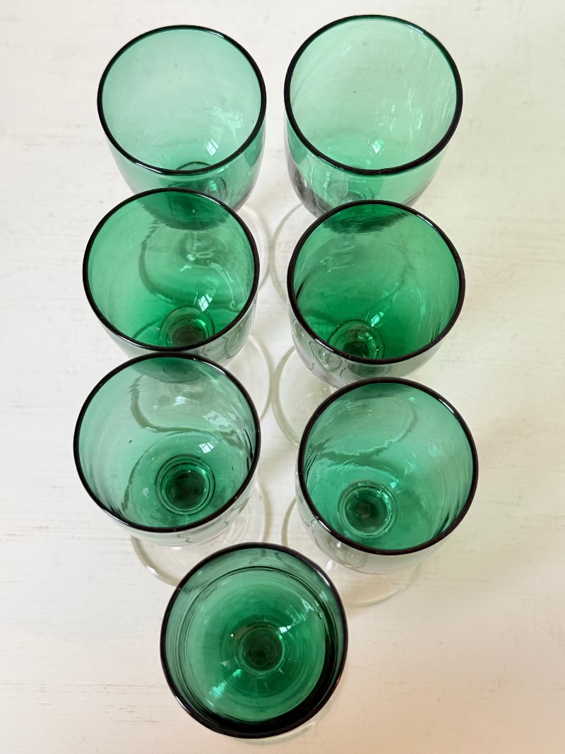 Set of seven antique Bristol green glasses with clear stems and emerald bowls, photographed on white surface.