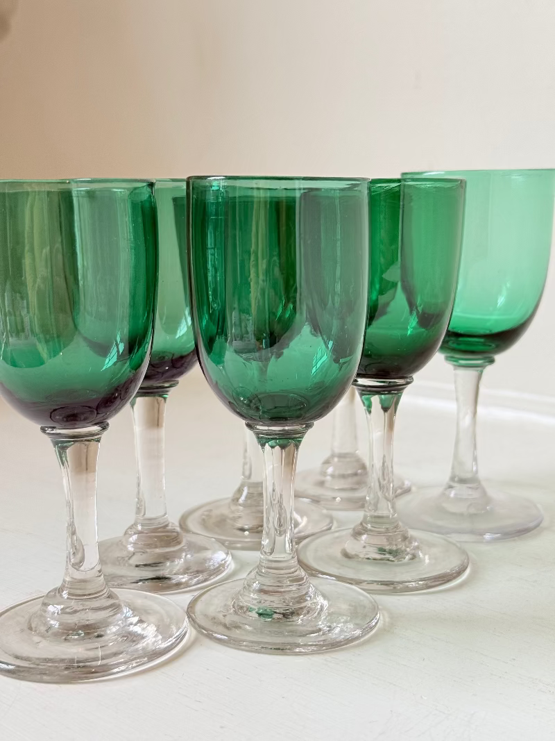 Set of seven antique Bristol green glasses with clear stems and emerald bowls, photographed on white surface.