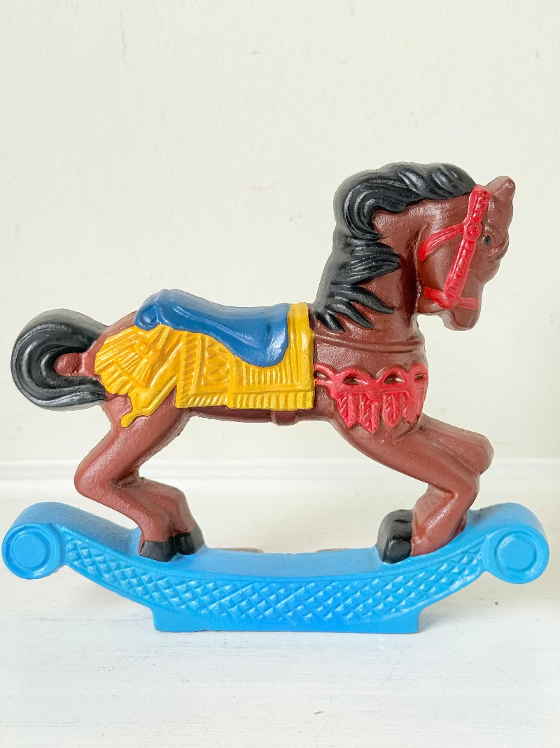 Vintage cast iron rocking horse doorstop with painted finish in red, yellow, blue, and black, photographed on a white surface