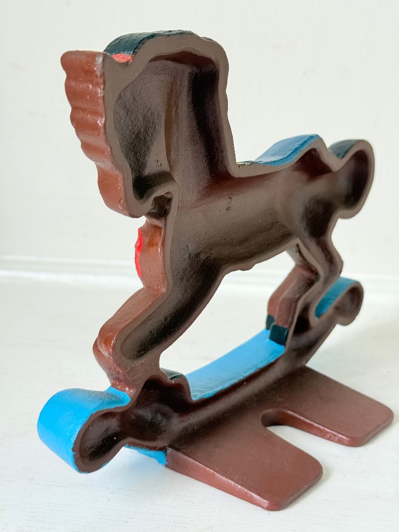 Vintage cast iron rocking horse doorstop with painted finish in red, yellow, blue, and black, photographed on a white surface