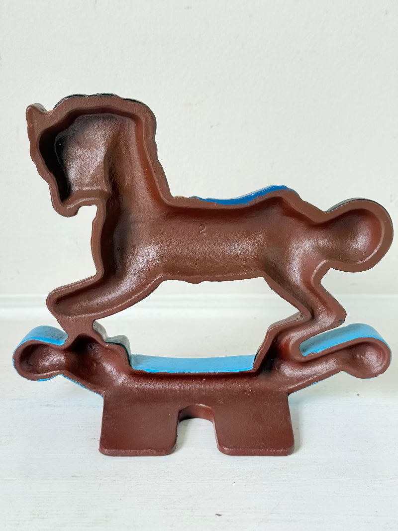 Vintage cast iron rocking horse doorstop with painted finish in red, yellow, blue, and black, photographed on a white surface