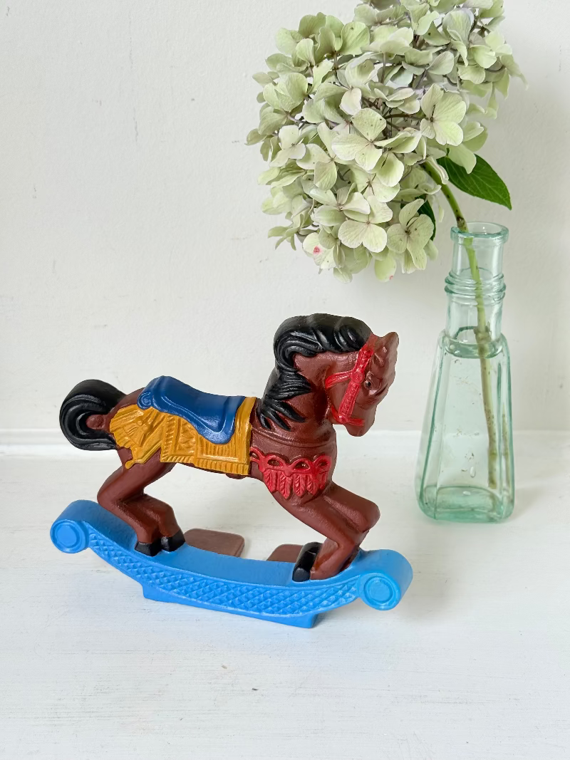 Vintage cast iron rocking horse doorstop with painted finish in red, yellow, blue, and black, photographed on a white surface