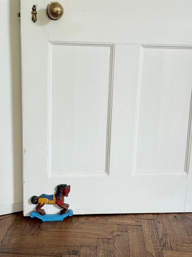 Vintage cast iron rocking horse doorstop with painted finish in red, yellow, blue, and black, photographed on a white surface