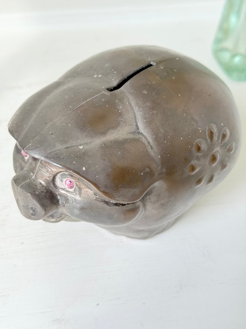 Vintage cast metal piggy bank in the shape of a pig with red painted eyes, photographed on a white surface