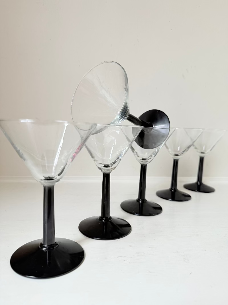 Set of six clear martini glasses with black stems, photographed on a white surface