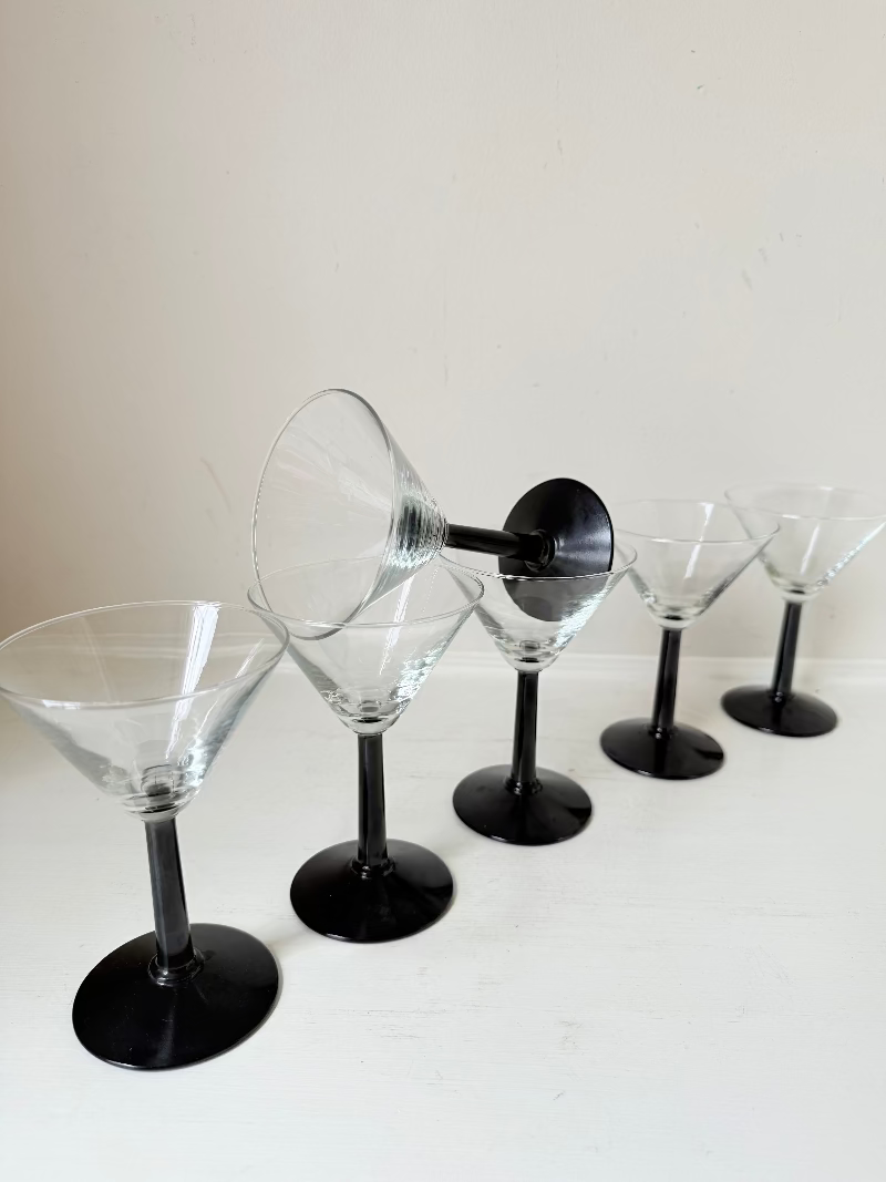 Set of six clear martini glasses with black stems, photographed on a white surface